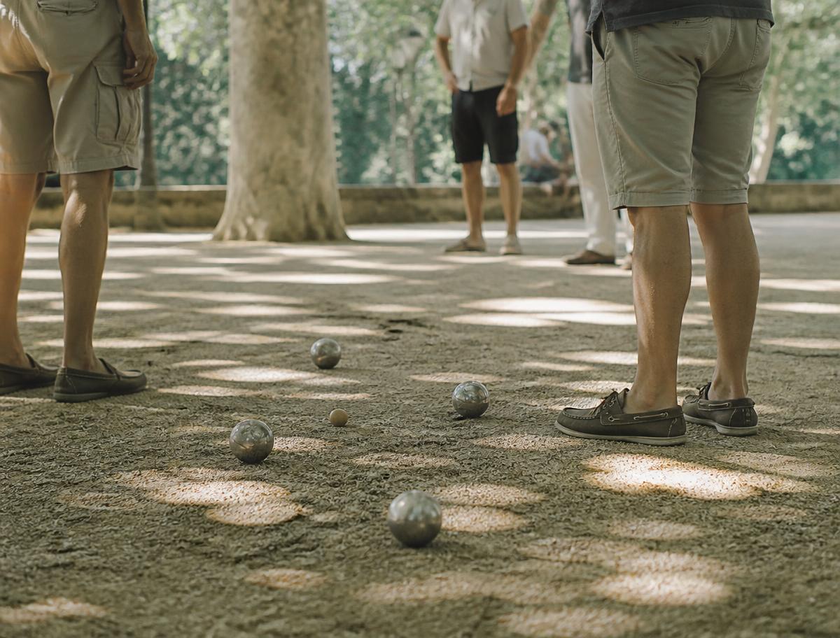 Boules de pétanque sur un terrain en gravier ombragé, joueurs autour du cochonnet