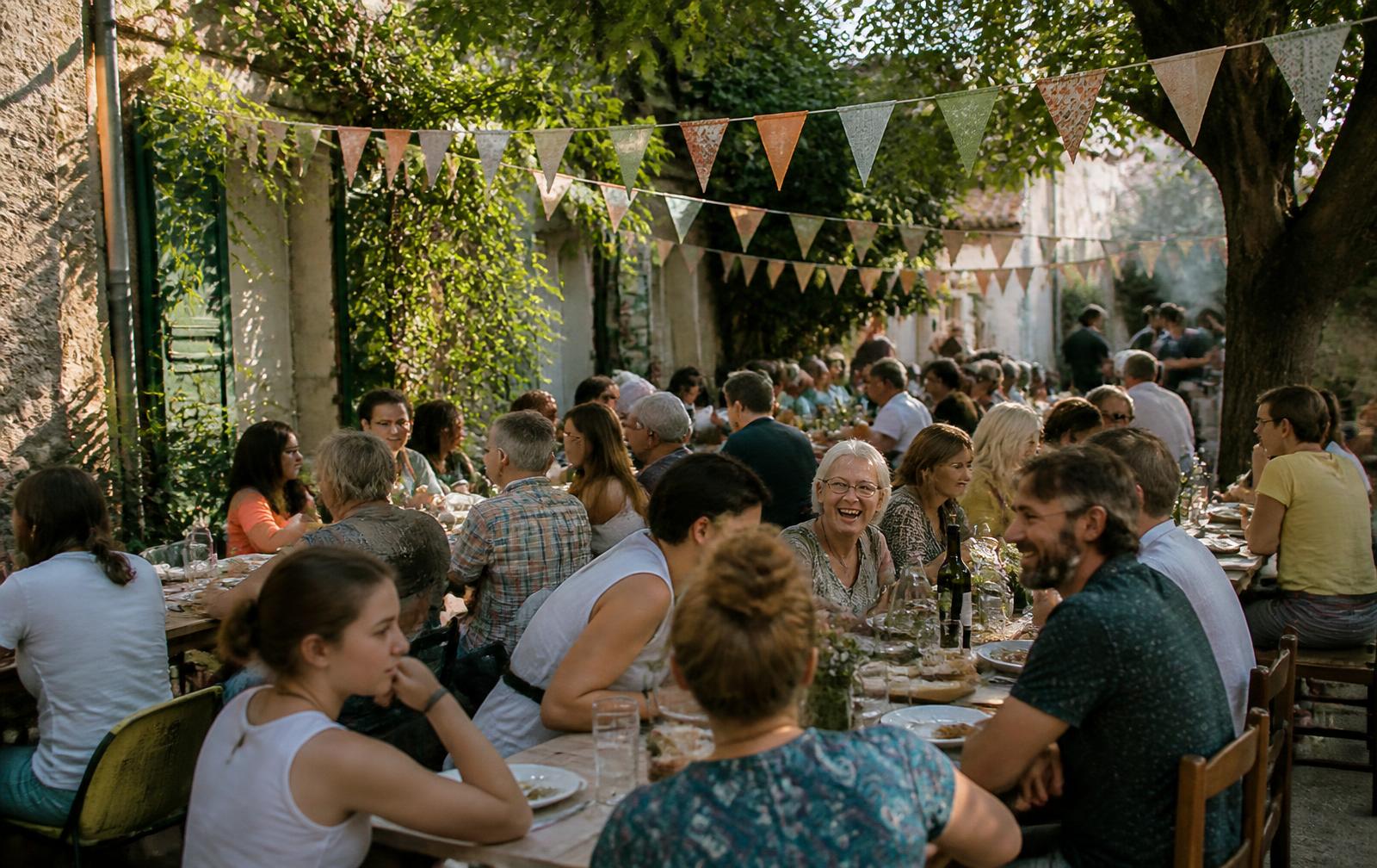 Longues tablées de voisins attablés sous les fanions lors d'une fête de quartier